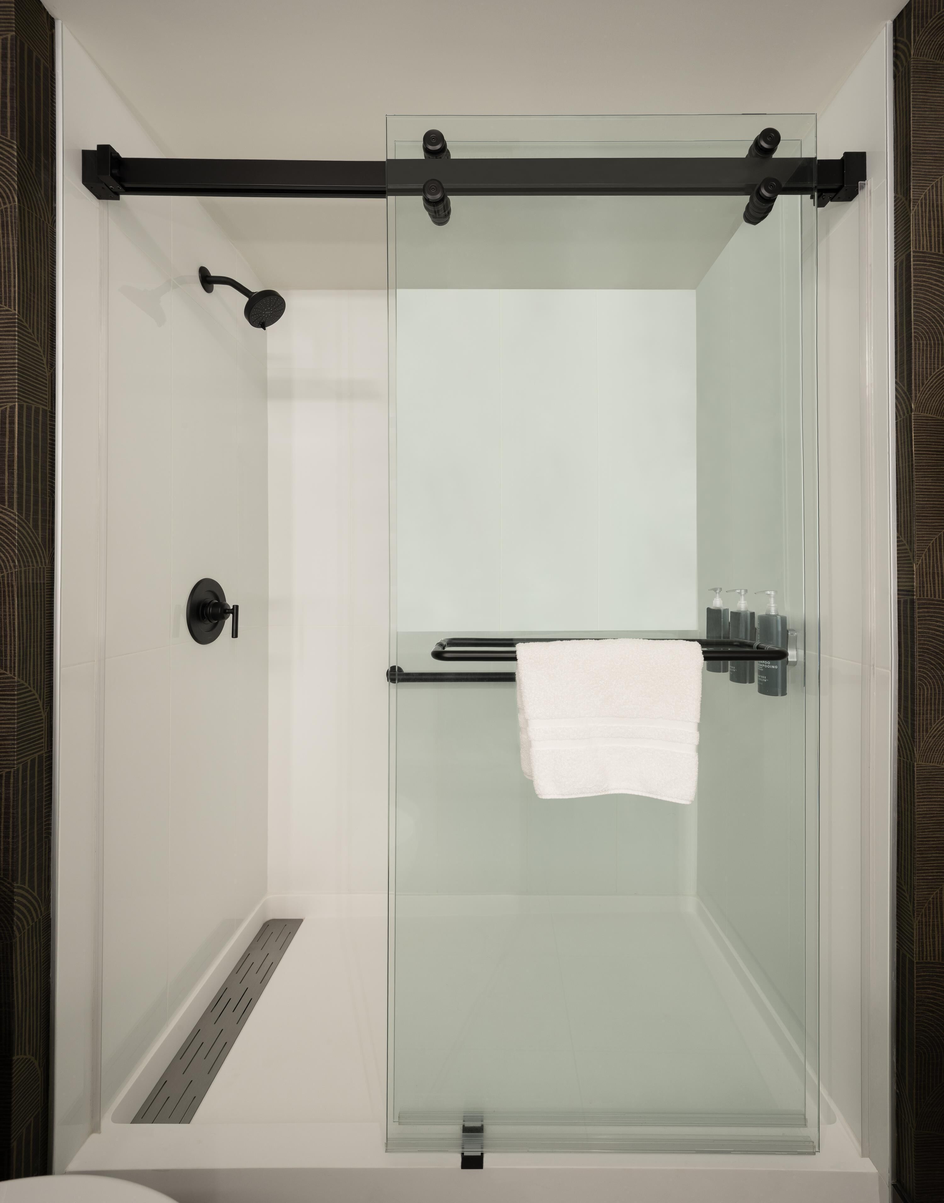 A glass-enclosed shower with a towel rack and toiletries.