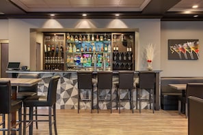 A bar area with a counter, shelves of bottles, glasses, and a seating area with chairs and tables. - DoubleTree by Hilton North Vancouver (North Vancouver)