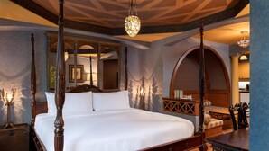 A four-poster bed with a canopy, a wooden nightstand, a mirror, and a chandelier.