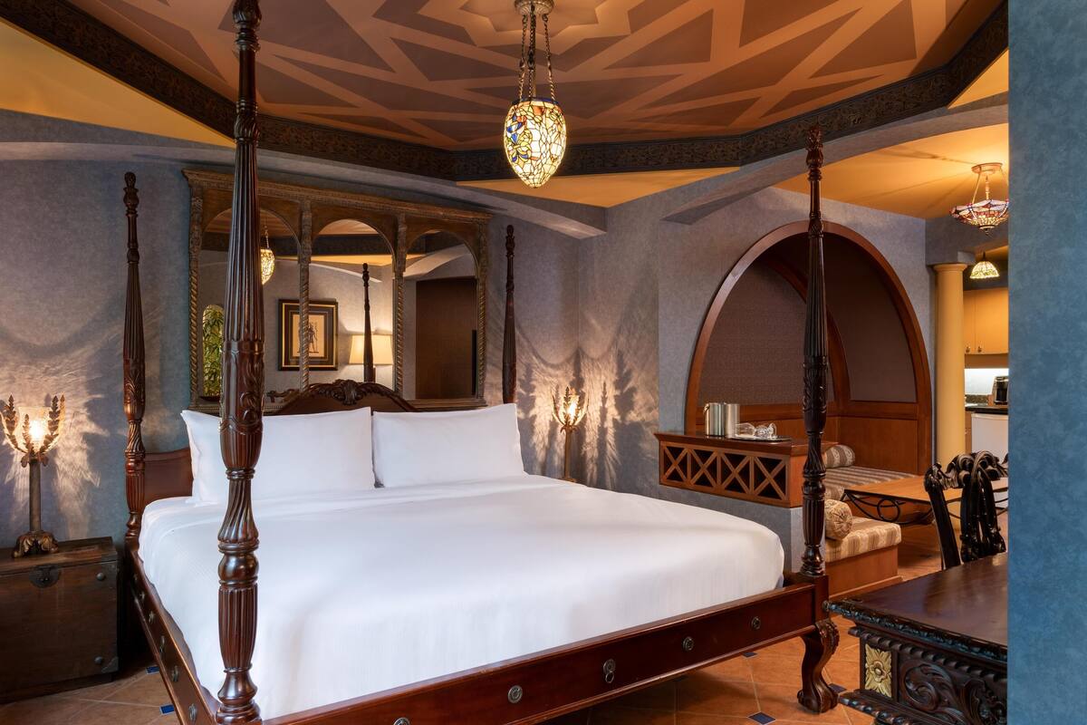 A four-poster bed with a canopy, a wooden nightstand, a mirror, and a chandelier.