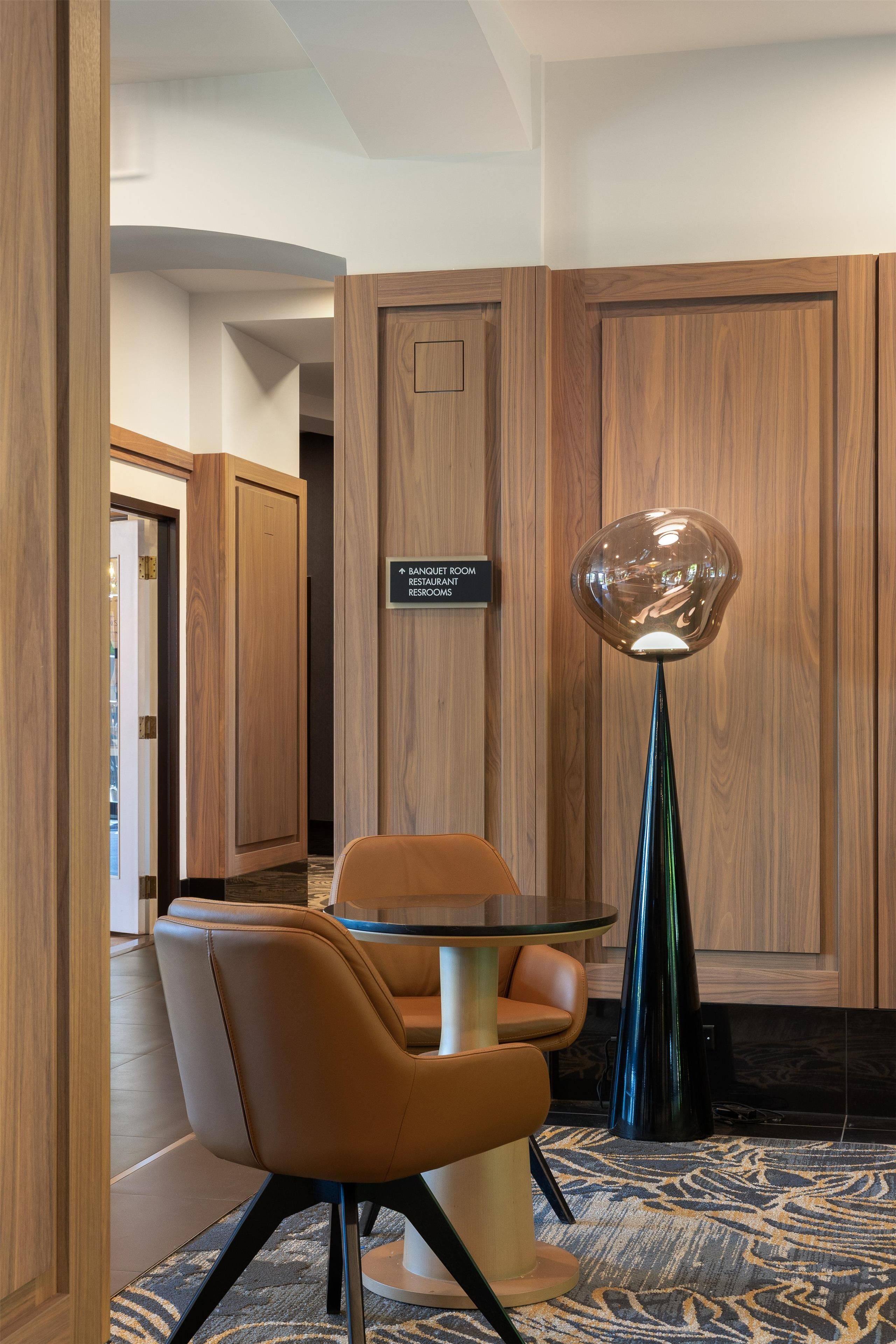 A hotel room with a dining area, a modern floor lamp, and a sign indicating the location of the banquet room, restaurant, and restroom.