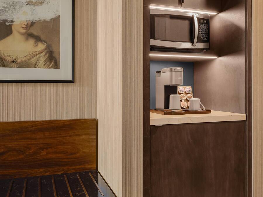 A compact room with a bed, a small wooden cabinet, a microwave, a coffee maker, and a framed picture on the wall.