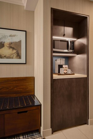 A compact room with a bed, a small wooden cabinet, a microwave, a coffee maker, and a framed picture on the wall. - DoubleTree by Hilton North Vancouver (North Vancouver)