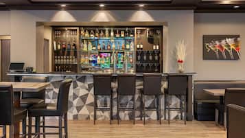 A bar area with a counter, shelves of bottles, glasses, and a seating area with chairs and tables.