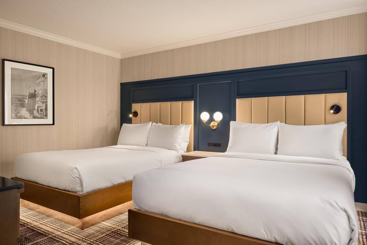 A hotel room with two beds, a framed picture on the wall, and a modern headboard design.