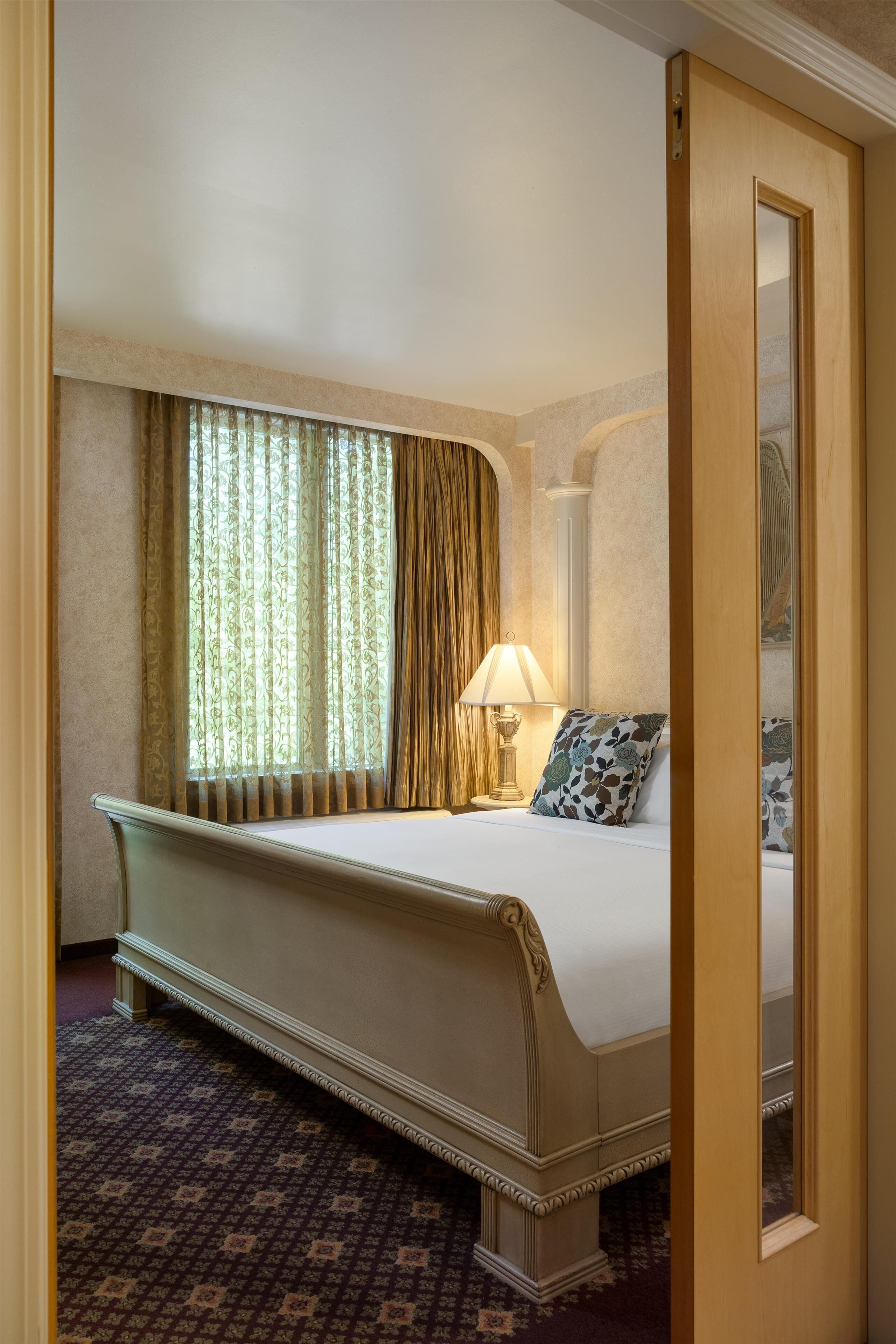 Una habitación de hotel con una cama grande, una mesita de noche, una lámpara y un espejo.