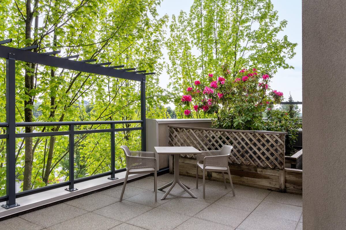 An outdoor patio with a table and chairs, a pergola, and a view of trees and flowers.