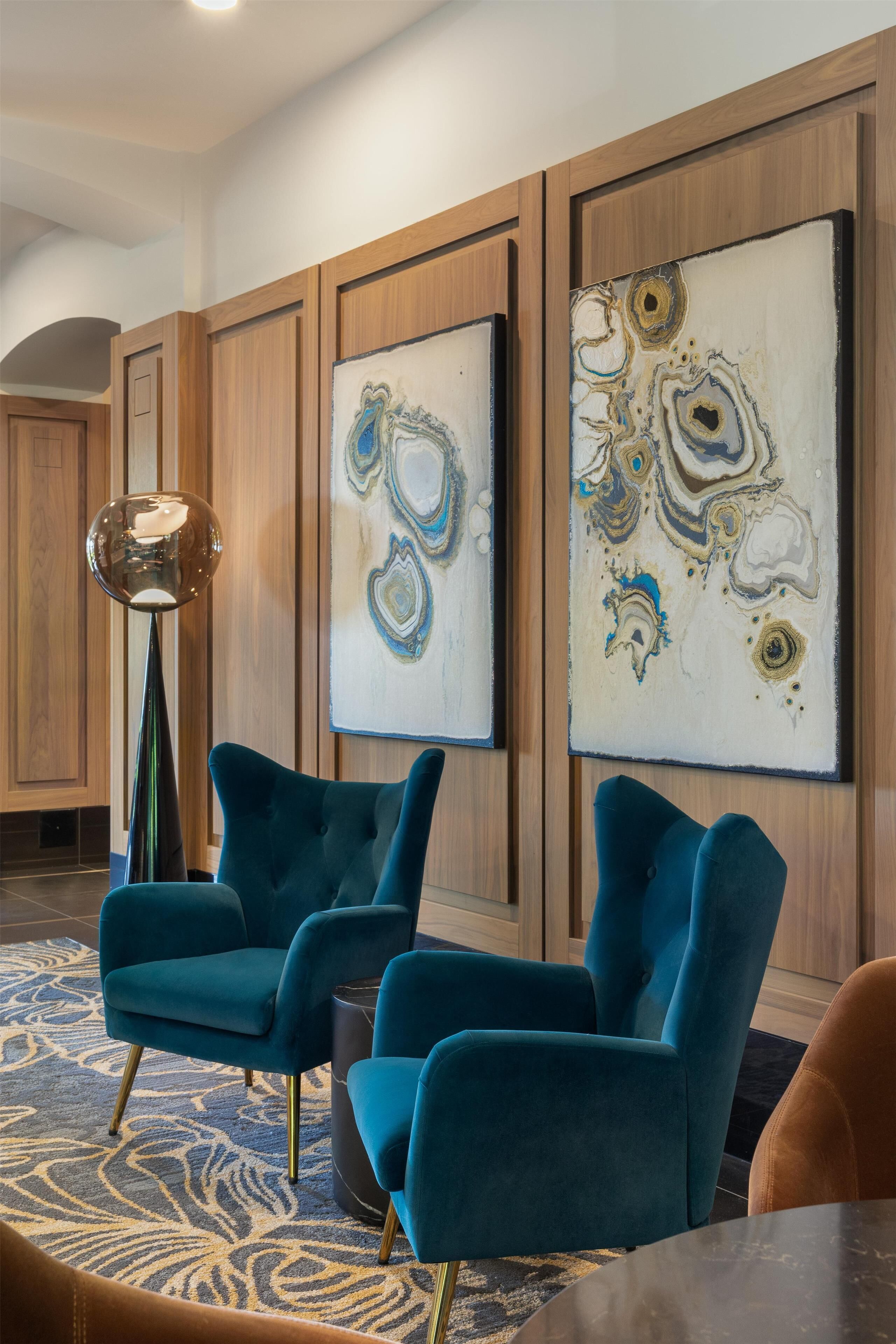 Un hall d’entrée moderne avec des fauteuils turquoise, des œuvres d’art abstraites accrochées au mur et un grand lampadaire.