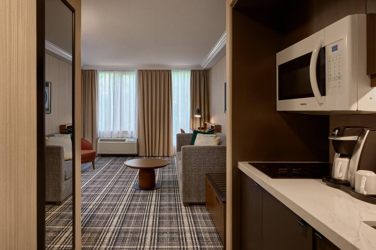 A hotel room with a kitchenette, a sofa, a dining table, and a view of the outdoors.