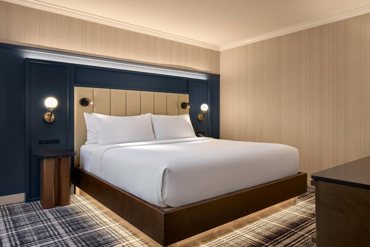 A hotel room with a bed, bedside tables, and wall-mounted lamps.
