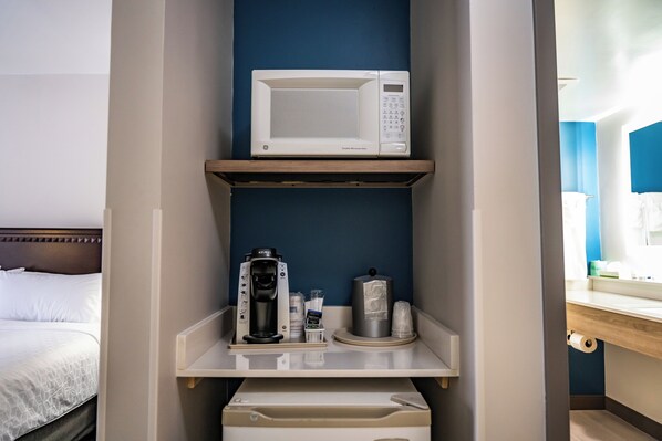 A hotel room with a microwave on a shelf, a coffee maker, and a small trash bin.