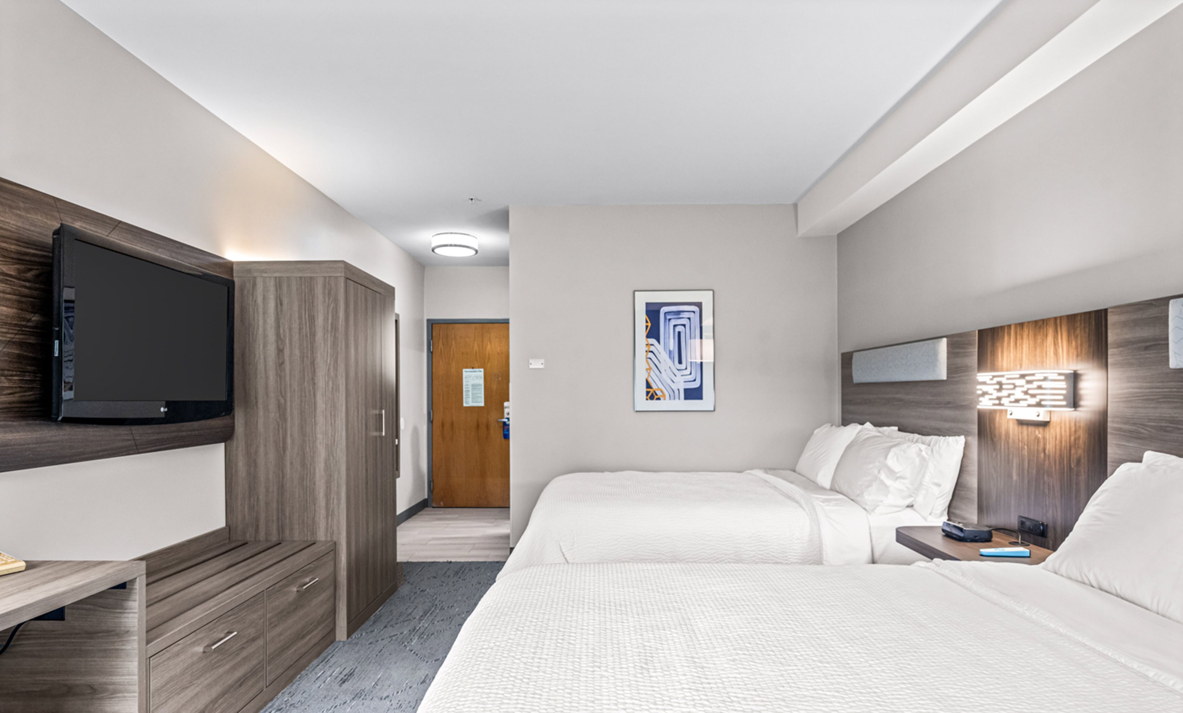A hotel room with a bed, a desk, a TV, and a door.