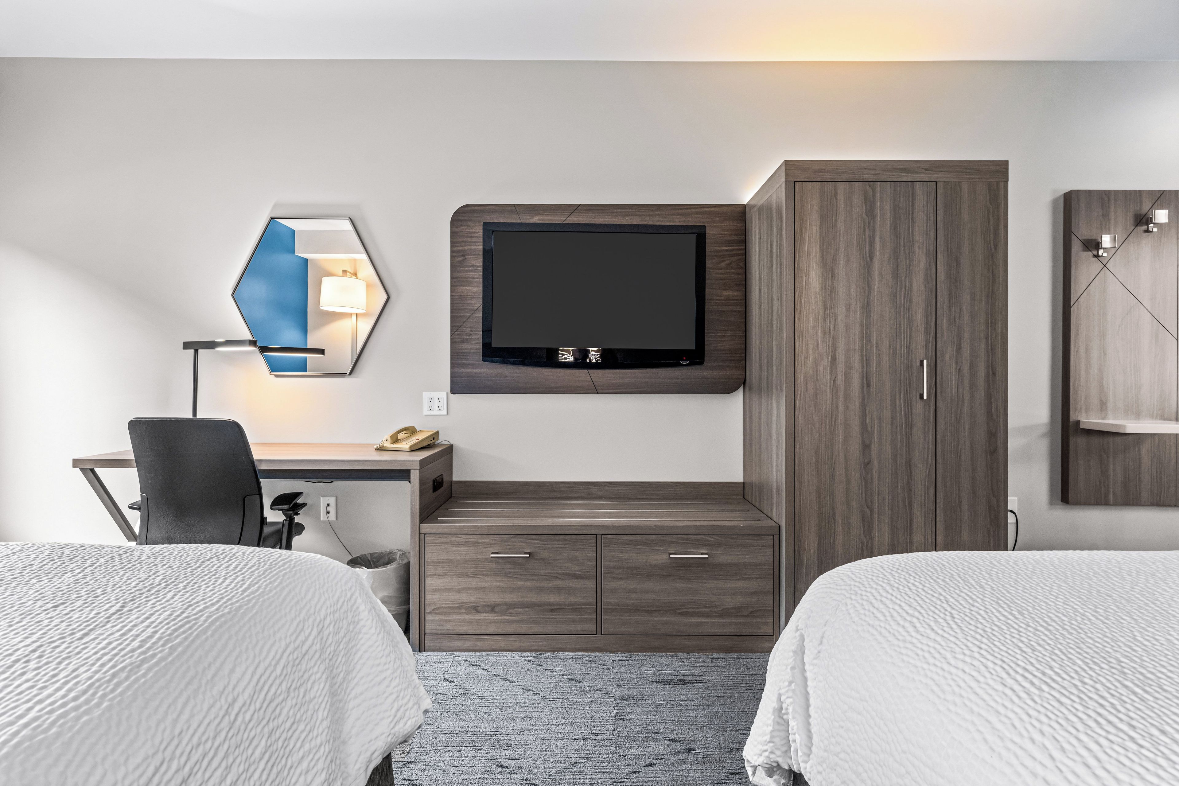 Quarto de hotel com cama, escrivaninha com cadeira, televisão fixada na parede e guarda-roupa.