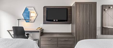Quarto de hotel com cama, escrivaninha com cadeira, televisão fixada na parede e guarda-roupa.