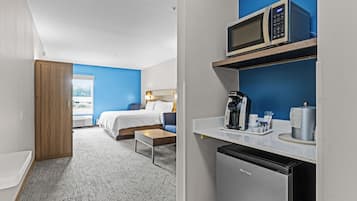A hotel room with a bed, a desk, a microwave, a coffee maker, and a dishwasher.