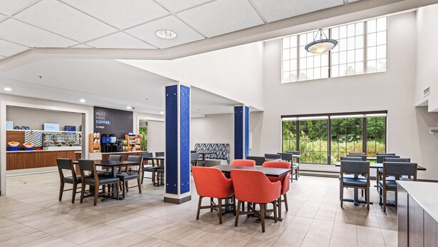 A spacious indoor area with multiple tables and chairs, a coffee station, and large windows providing natural light. - Holiday Inn Express Hotel & Suites Carneys Point by IHG (Penns Grove)
