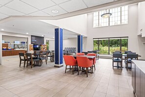A spacious indoor area with multiple tables and chairs, a coffee station, and large windows providing natural light.