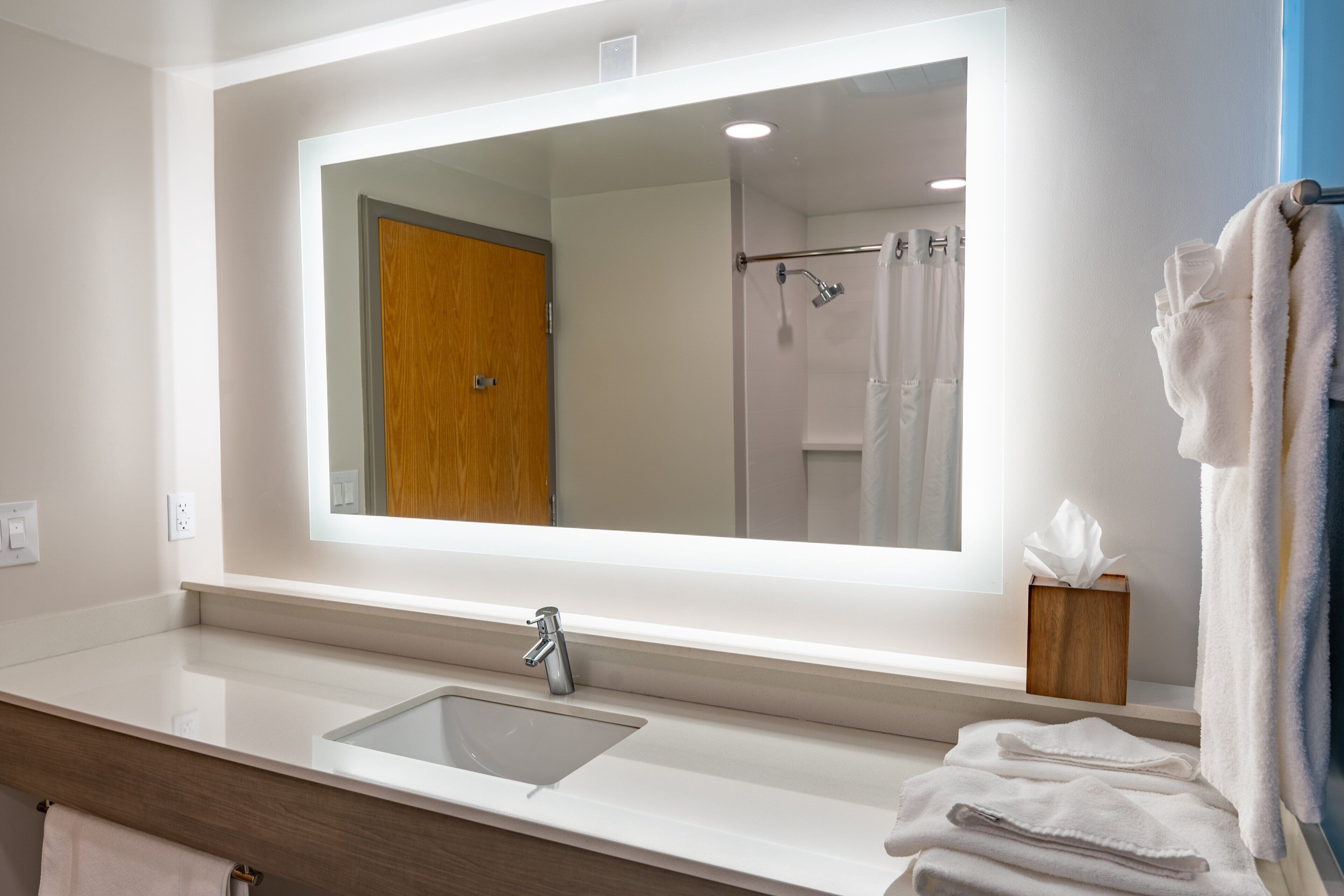 Une salle de bain avec un grand miroir, un lavabo et un porte-serviettes avec des serviettes.