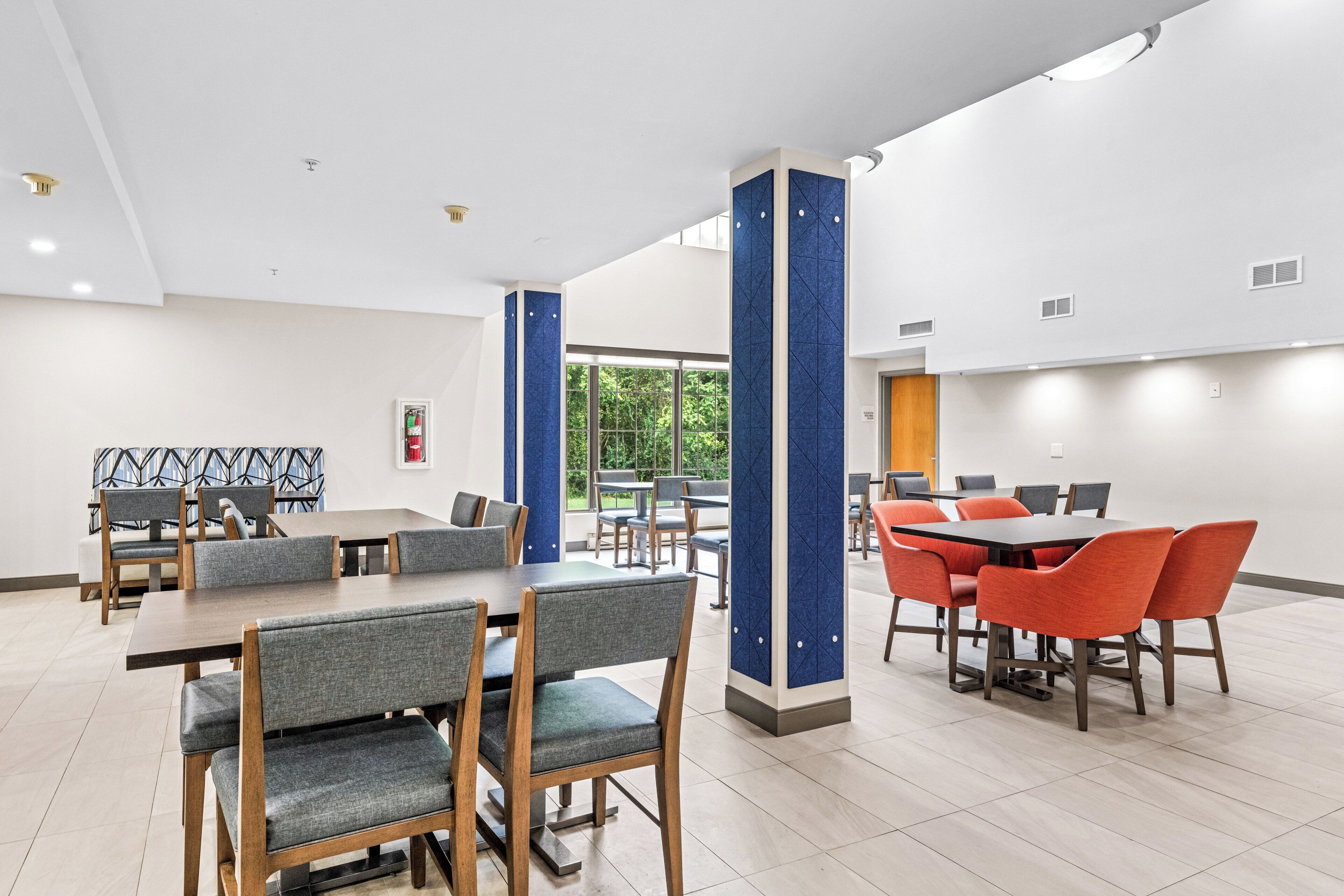 A modern dining area with multiple tables and chairs, large windows, and a clean, white interior.