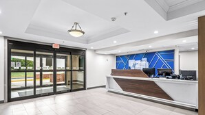 A modern reception area with a glass door entrance, a reception desk with computers, and a blue geometric wall design. - Holiday Inn Express Hotel & Suites Carneys Point by IHG (Penns Grove)