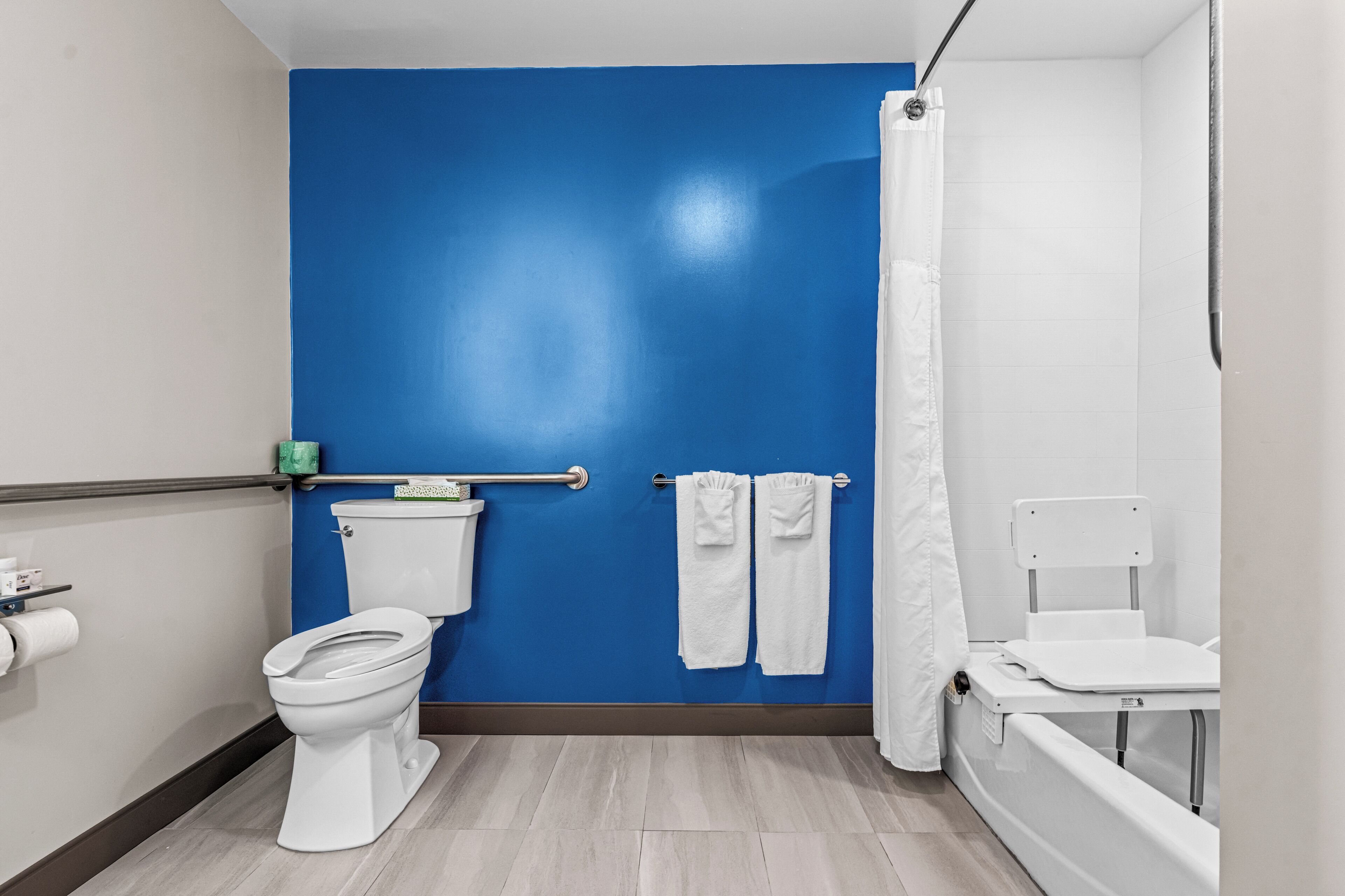 A bathroom with a blue wall, white toilet, white bathtub, and a shower curtain.