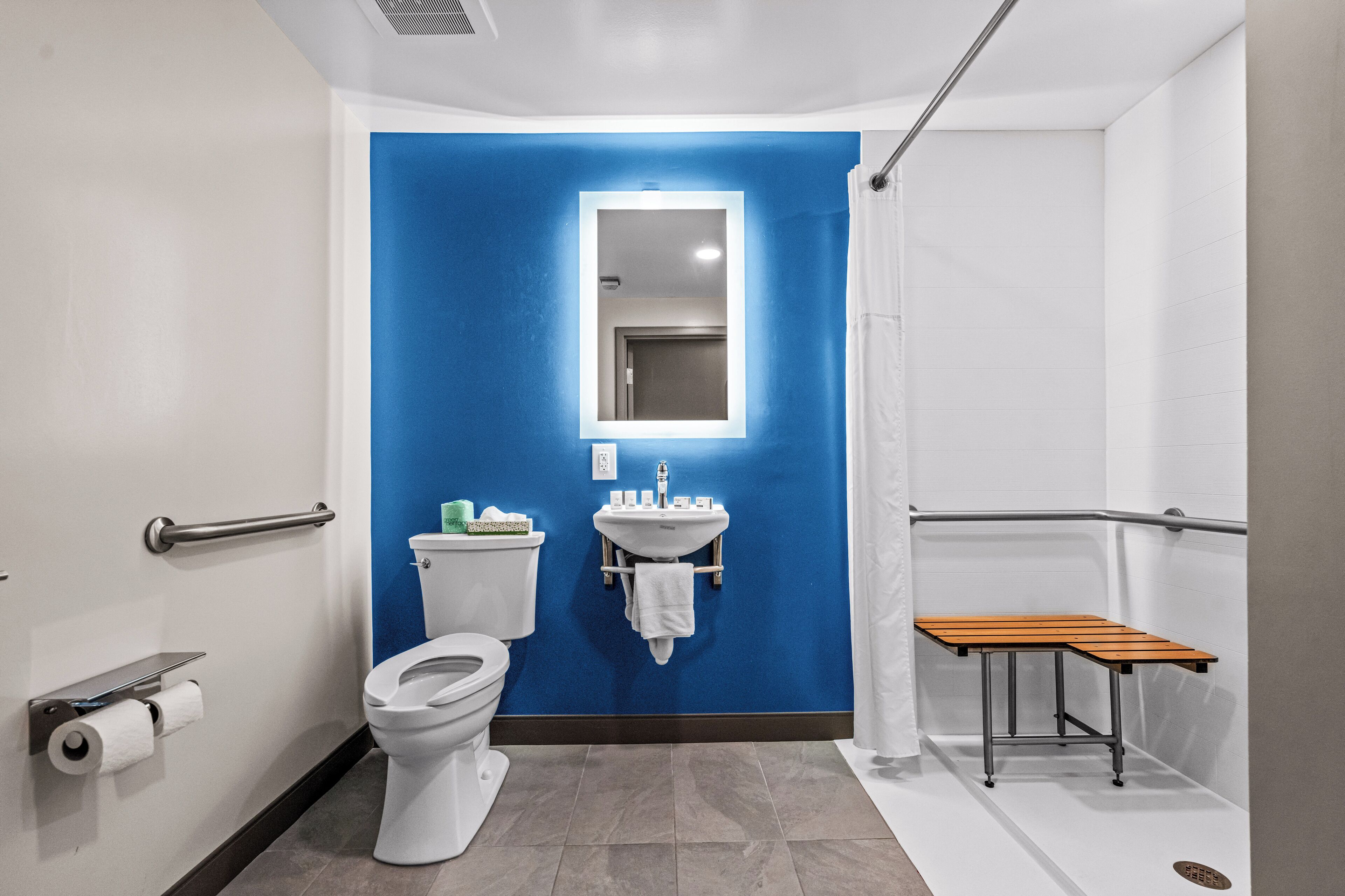 A bathroom with a blue accent wall, a white sink, a mirror, a toilet, and a wooden bench.