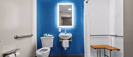 A bathroom with a blue accent wall, a white sink, a mirror, a toilet, and a wooden bench.