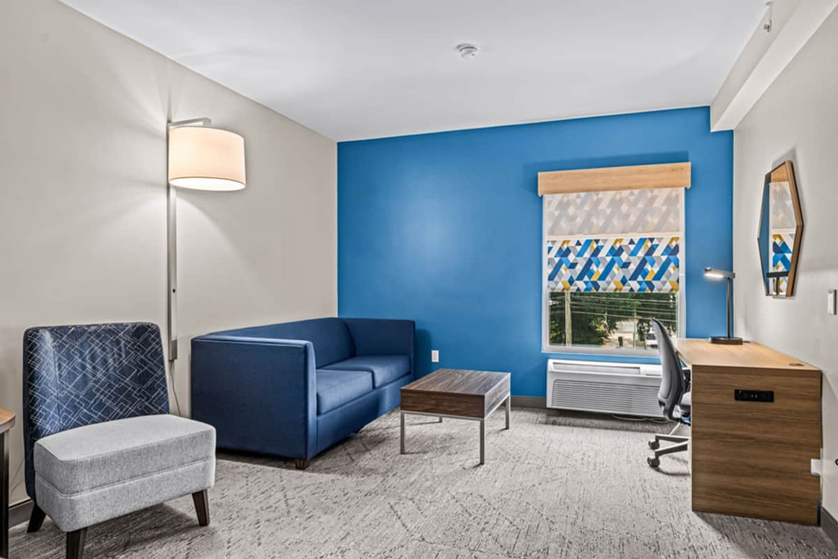 A hotel room with a blue accent wall, a sofa, a chair, a desk, and a lamp.