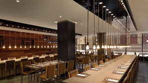A modern restaurant with long tables, hanging light fixtures, and a wooden wall.