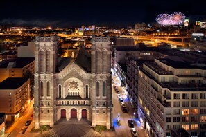 Una iglesia histórica con una cúpula central y dos torres, rodeada de edificios modernos y una calle concurrida de noche.