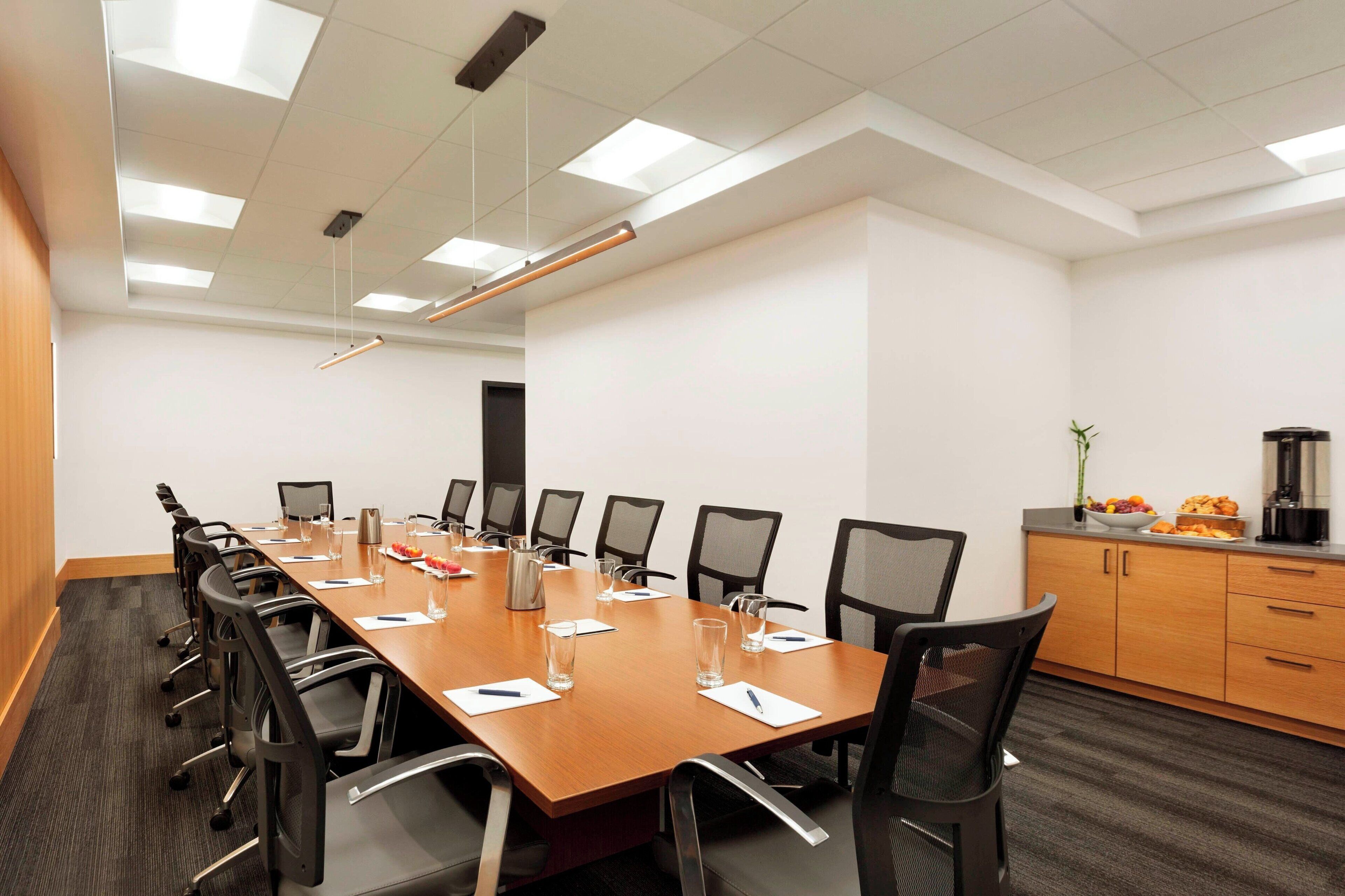 A conference room with a long table, chairs, a coffee machine, and a plant.