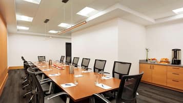 A conference room with a long table, chairs, a coffee machine, and a plant.
