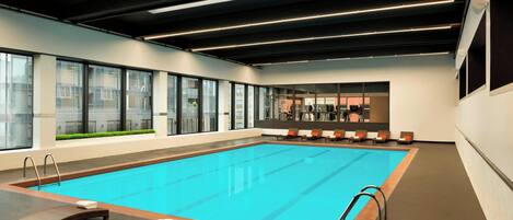 Una piscina interior moderna con paredes de vidrio transparente, sillones de descanso y un espacio para el gimnasio.