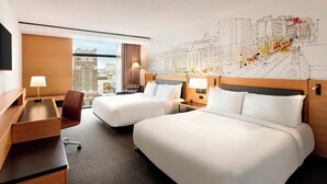 A hotel room with two beds, a desk, a chair, and a large window.