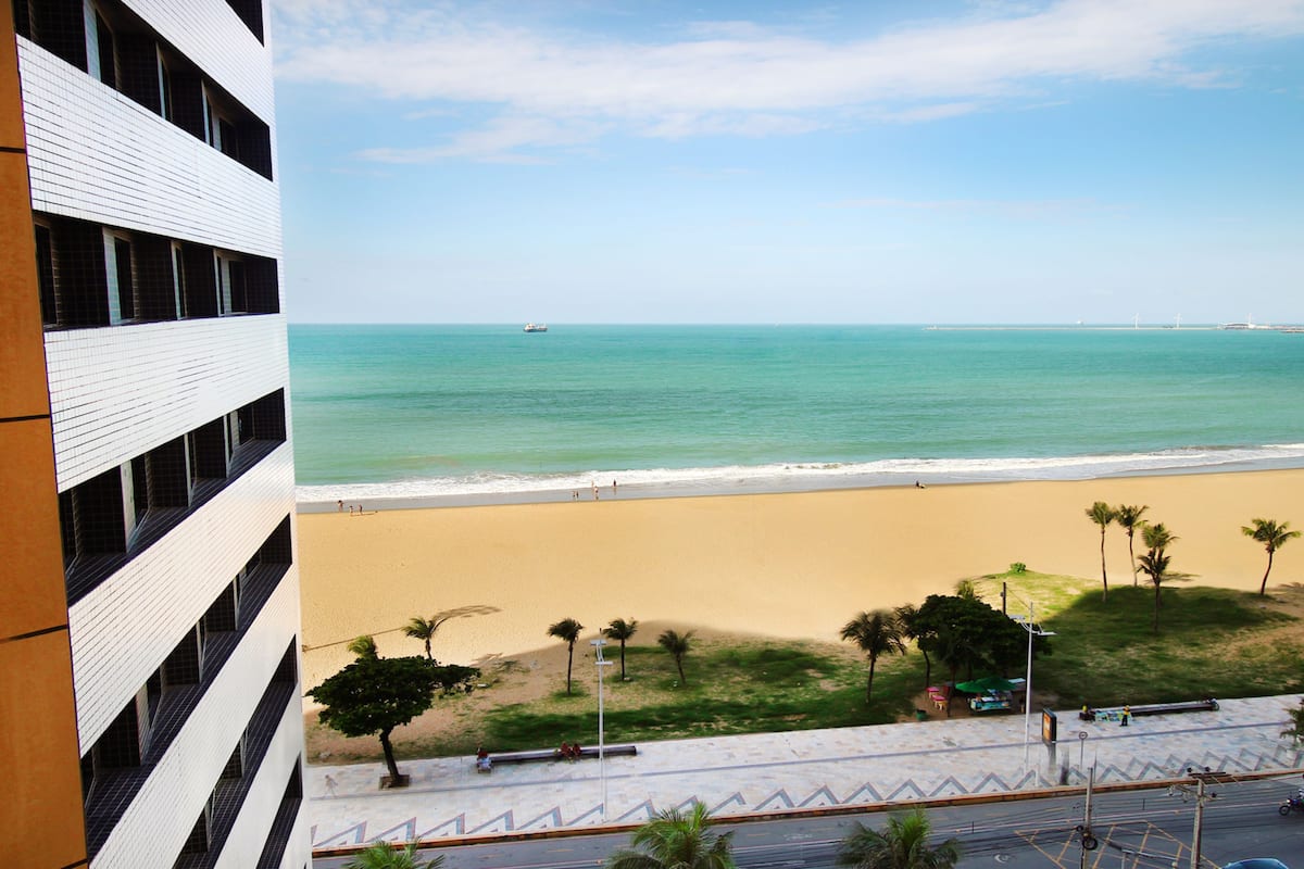 Vista da praia a partir de um edifício com fachada em azulejos, praia arenosa e palmeiras.