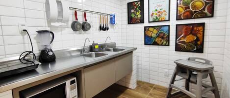 A modern kitchen with white tiles, stainless steel appliances, and a wooden floor.