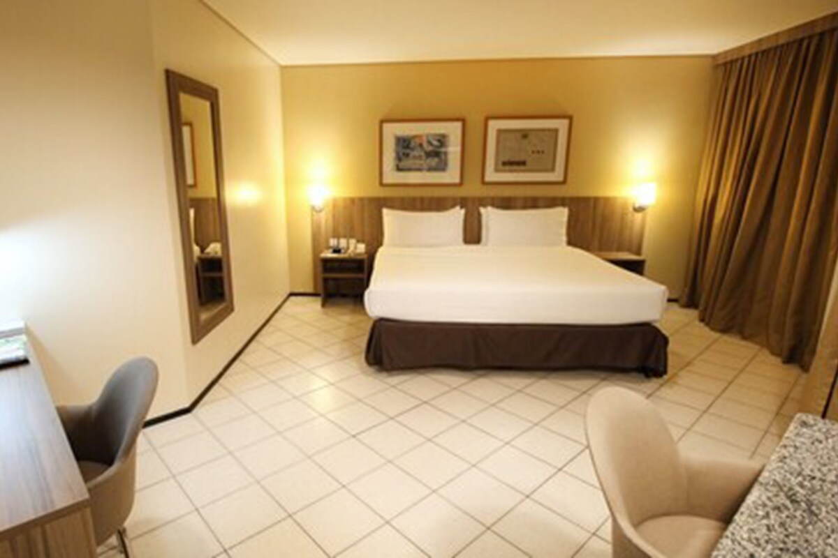 A hotel room with a bed, a desk, a chair, a TV, and two bedside lamps.