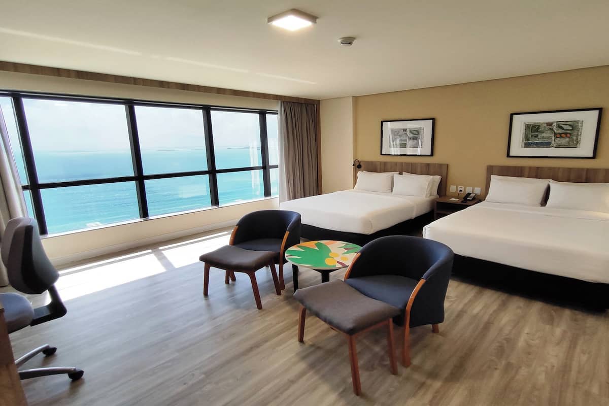 Quarto de hotel com duas camas, uma escrivaninha, uma cadeira e uma mesa pequena.
