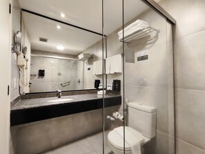 A modern bathroom with a glass shower enclosure, a sink with a granite countertop, a toilet, and a towel rack with folded towels.