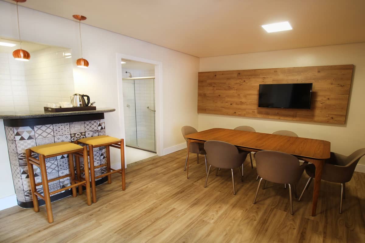 Uma cozinha moderna com uma mesa de jantar de madeira, banquetas e uma TV fixada na parede.