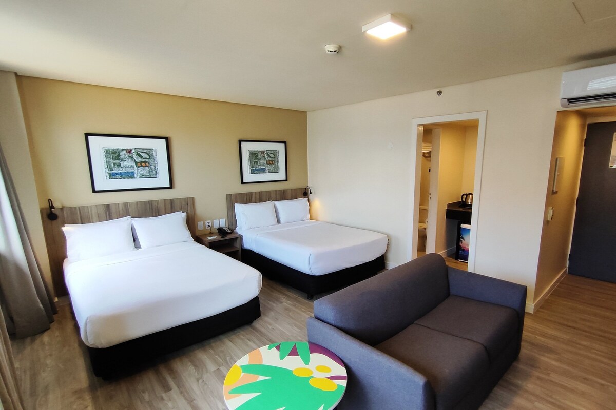 A hotel room with two beds, a sofa, a small round table, and a door leading to a bathroom.