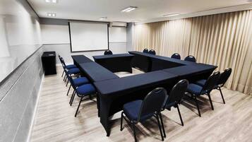 A conference room with a large rectangular table, blue chairs, a whiteboard, and a projector screen.