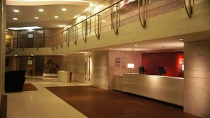 A modern hotel lobby with a reception desk, a staircase, and a seating area with a plant.