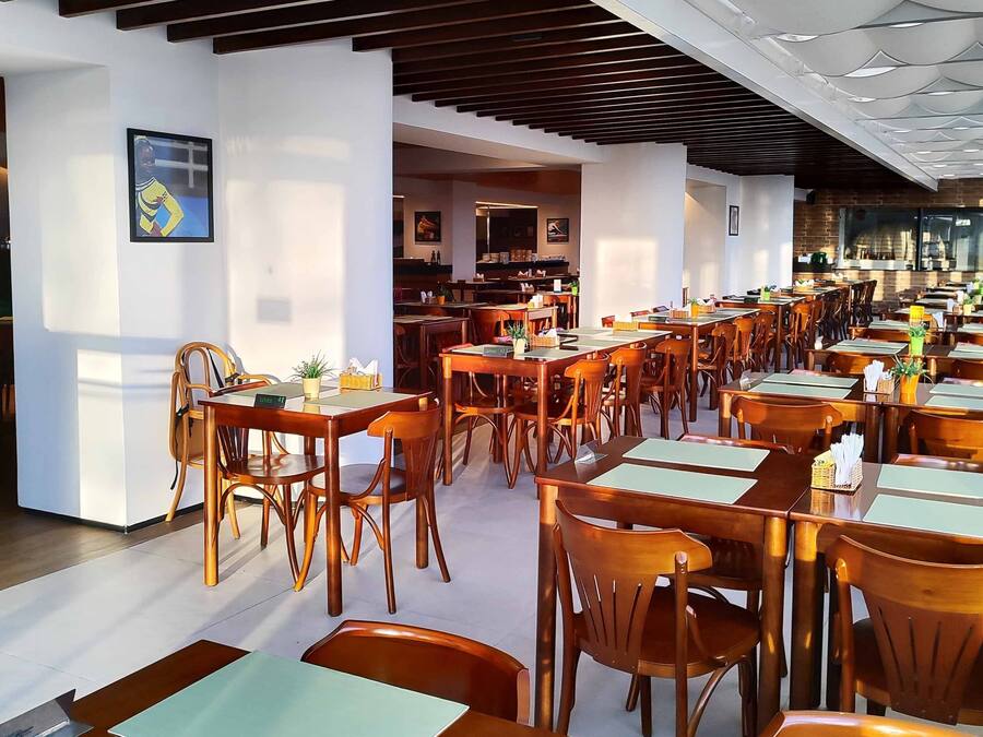 A spacious restaurant with wooden tables and chairs, a modern ceiling design, and framed artwork on the walls.