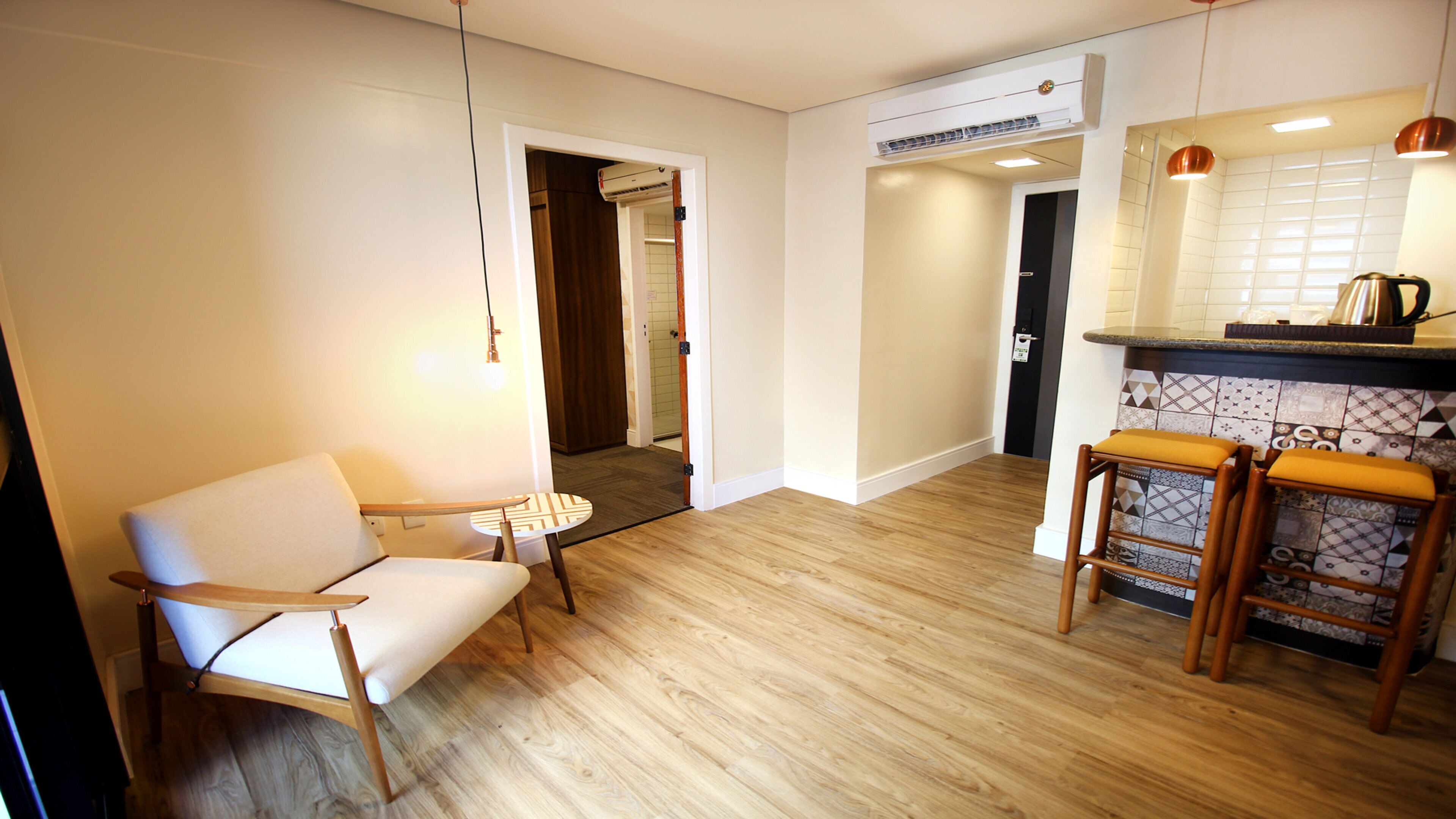 Une cuisine moderne avec un plancher en bois, un coin bar avec des tabourets et un espace détente avec une chaise et une table.