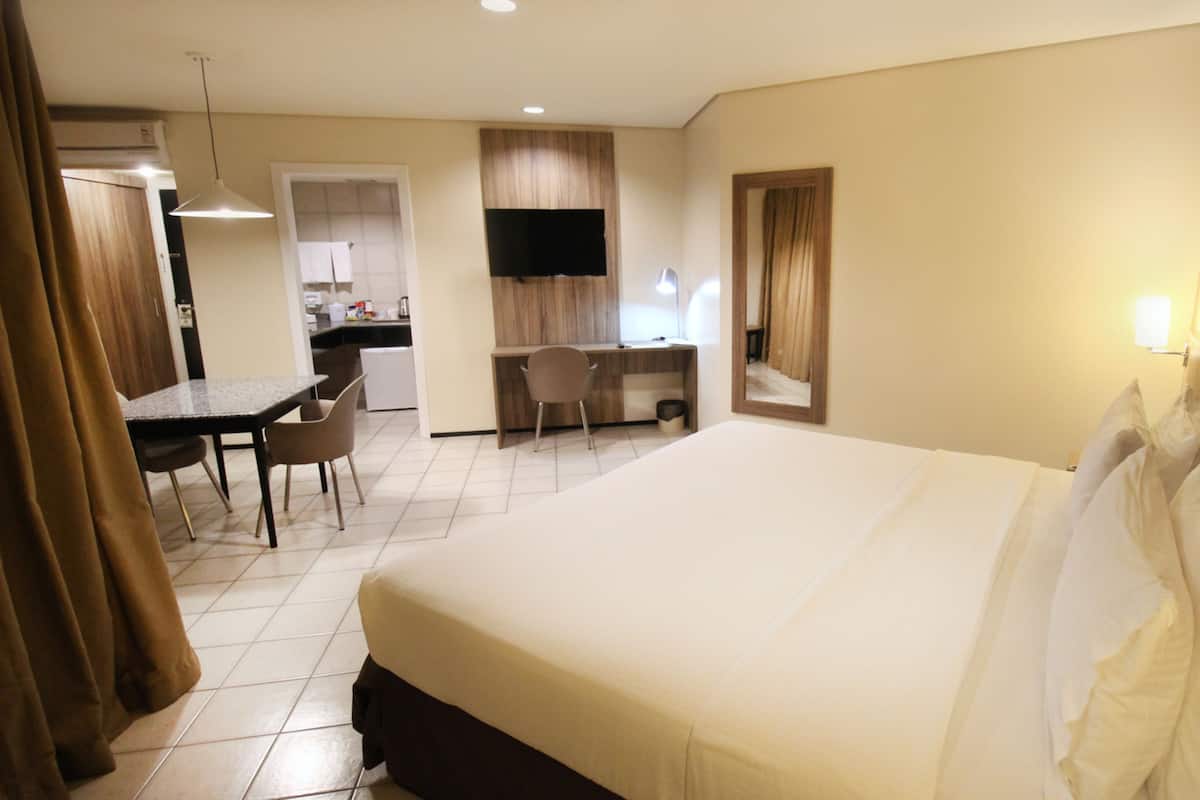 Quarto de hotel com uma cama grande, uma escrivaninha, uma cadeira e uma televisão.