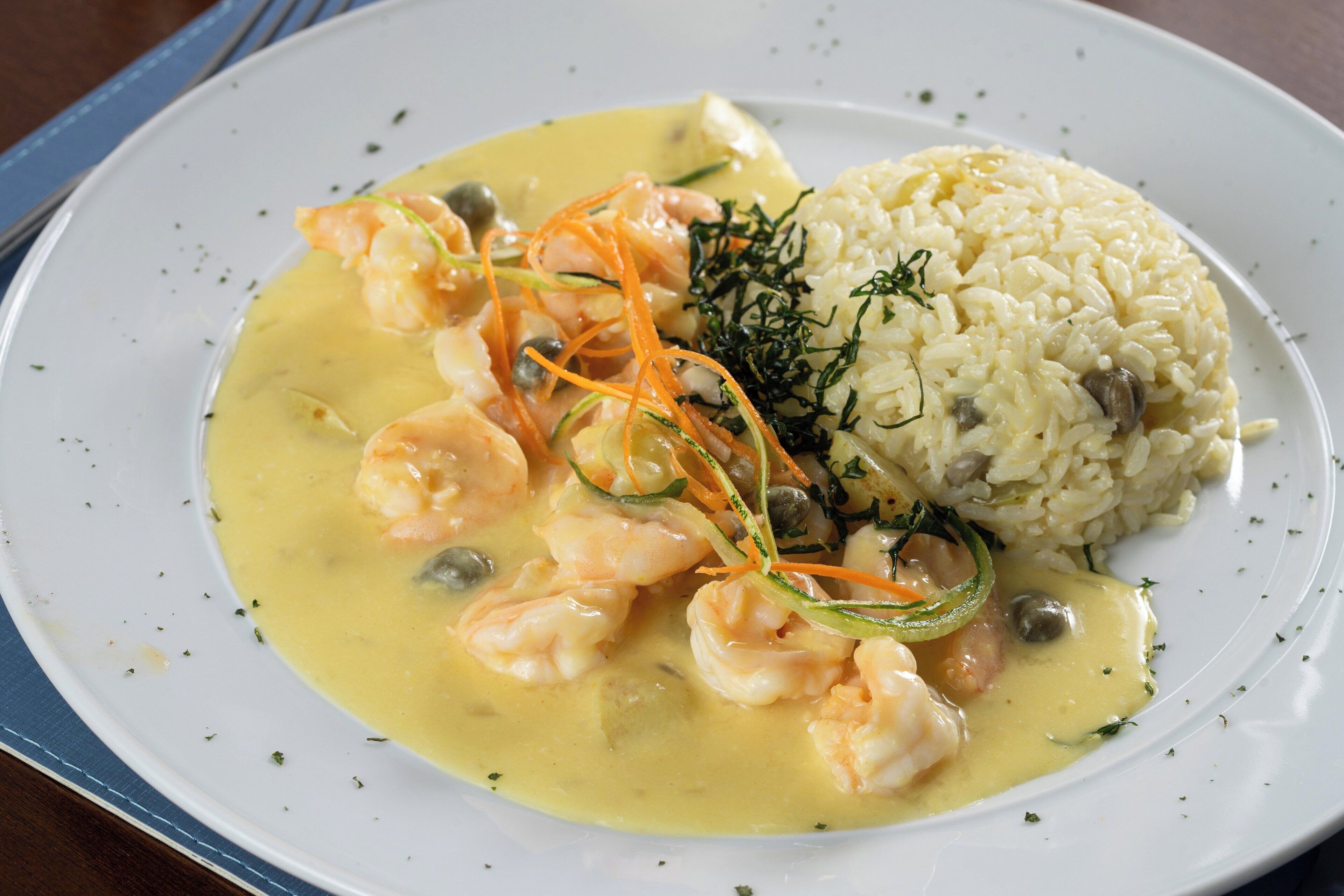 Une assiette de crevettes nappées d’une sauce crémeuse, servies avec du riz et des légumes.