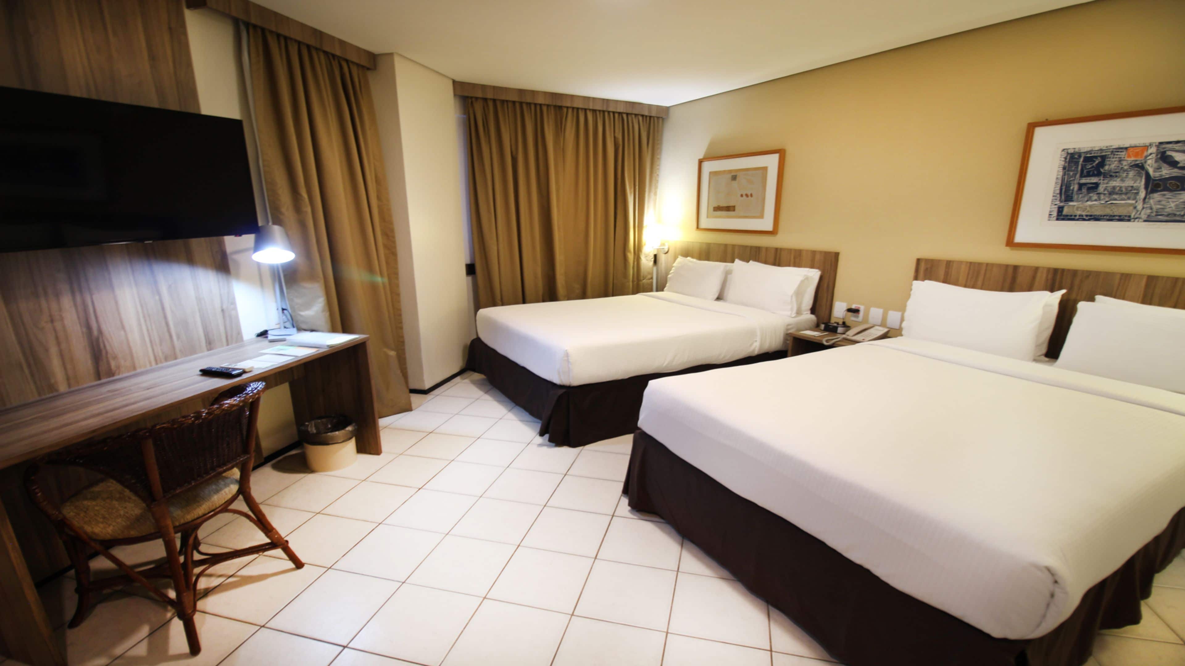 A hotel room with two beds, a desk with a chair, a television, and a framed picture on the wall.