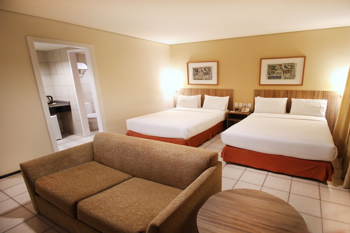 A hotel room with two beds, a sofa, a small table, and artwork on the walls.