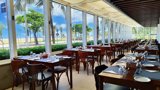 A restaurant with a long table layout, large windows, and a view of the beach. - Holiday Inn Fortaleza by IHG (Fortaleza)